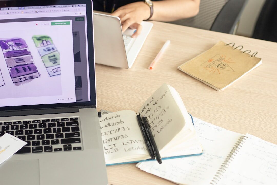 Hands typing on a laptop next to printed charts and a notebook